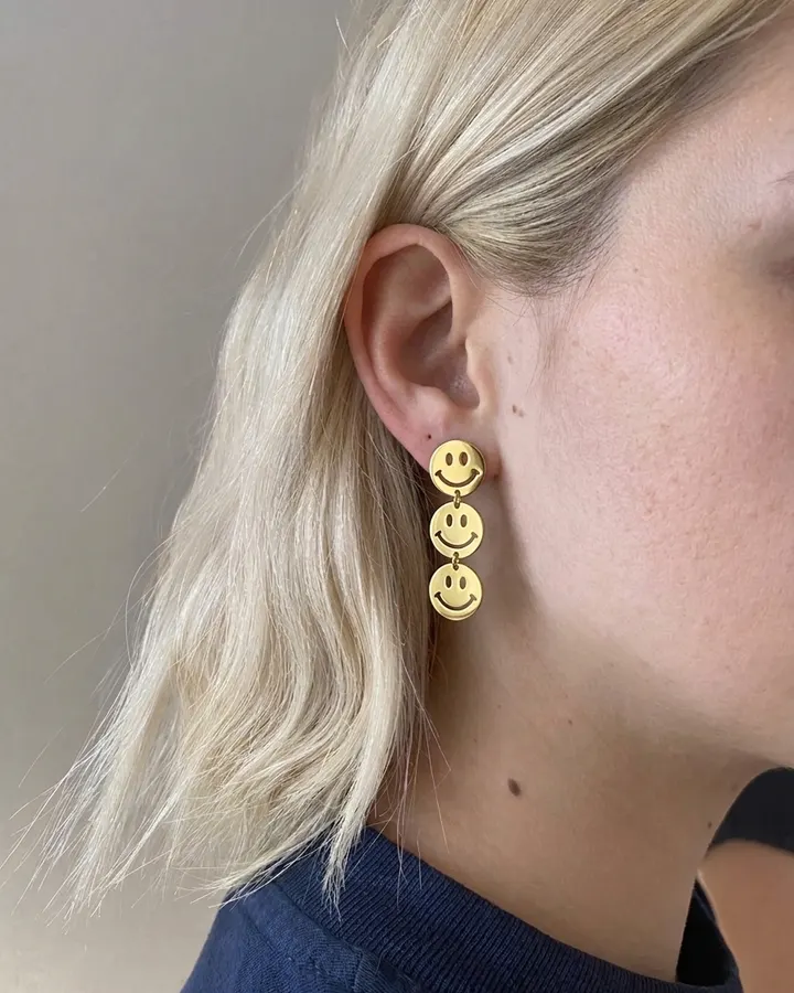 Gold smiley-face drop earring worn on an ear