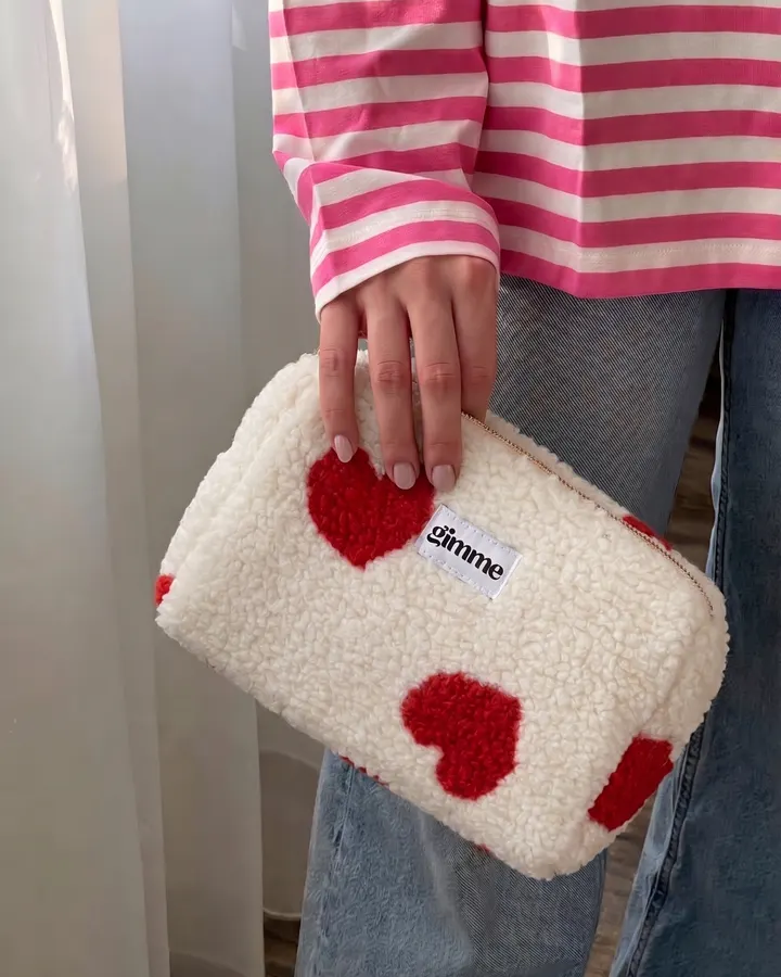 Cream teddy-fleece pouch with red hearts, held in one hand